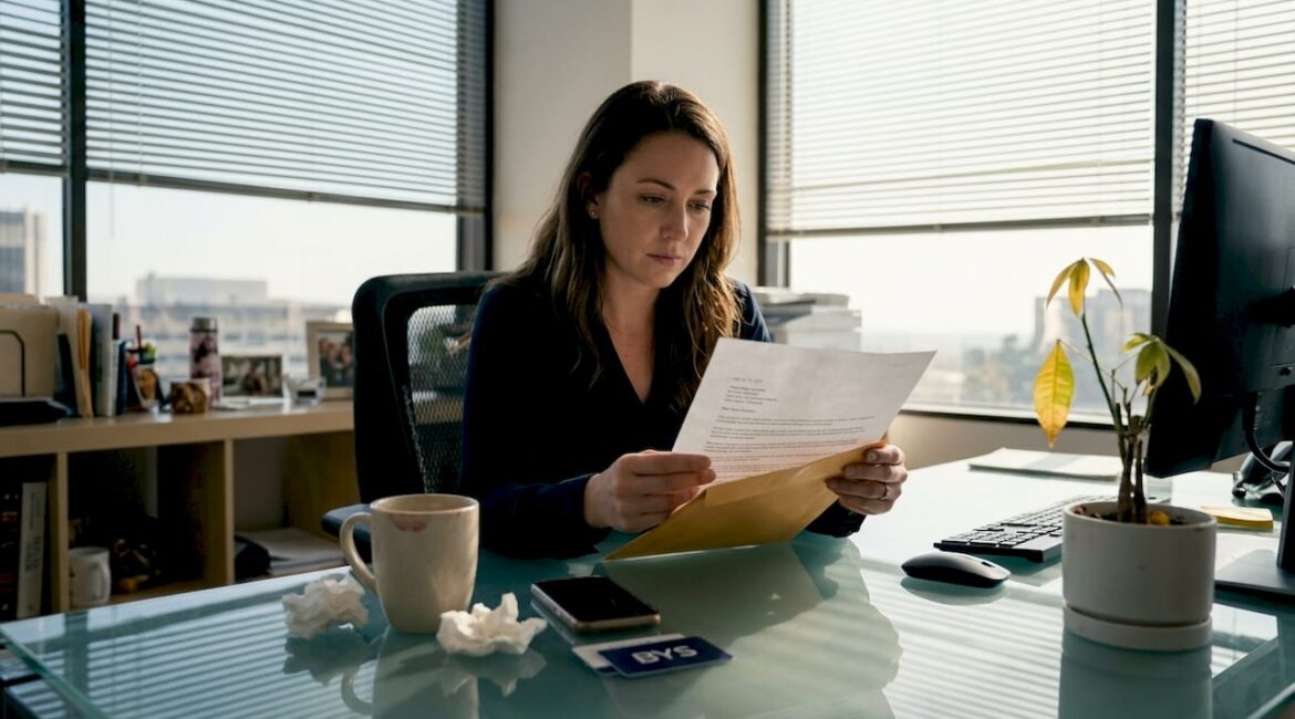 Media employee reading termination letter in corner office